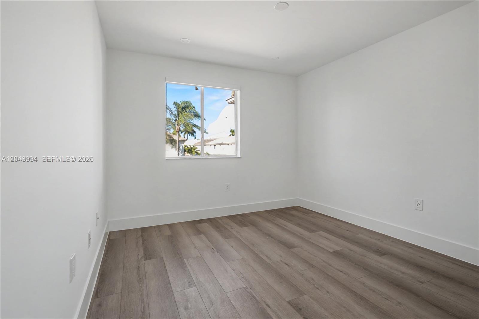 An empty room features white walls, wood-look flooring, and a single window — 16240 SW 75th St # 0, Miami FL 33193, MIAMI, FL