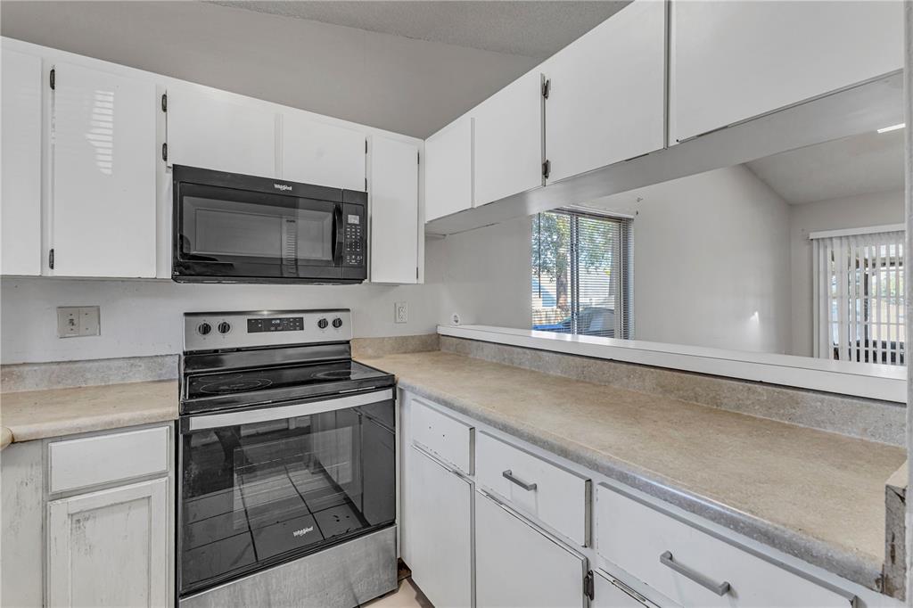 A kitchen with white cabinets, a black microwave and stove, and a pass-through window — 3675 WESTLAND COURT UNIT 1, ORLANDO, FL