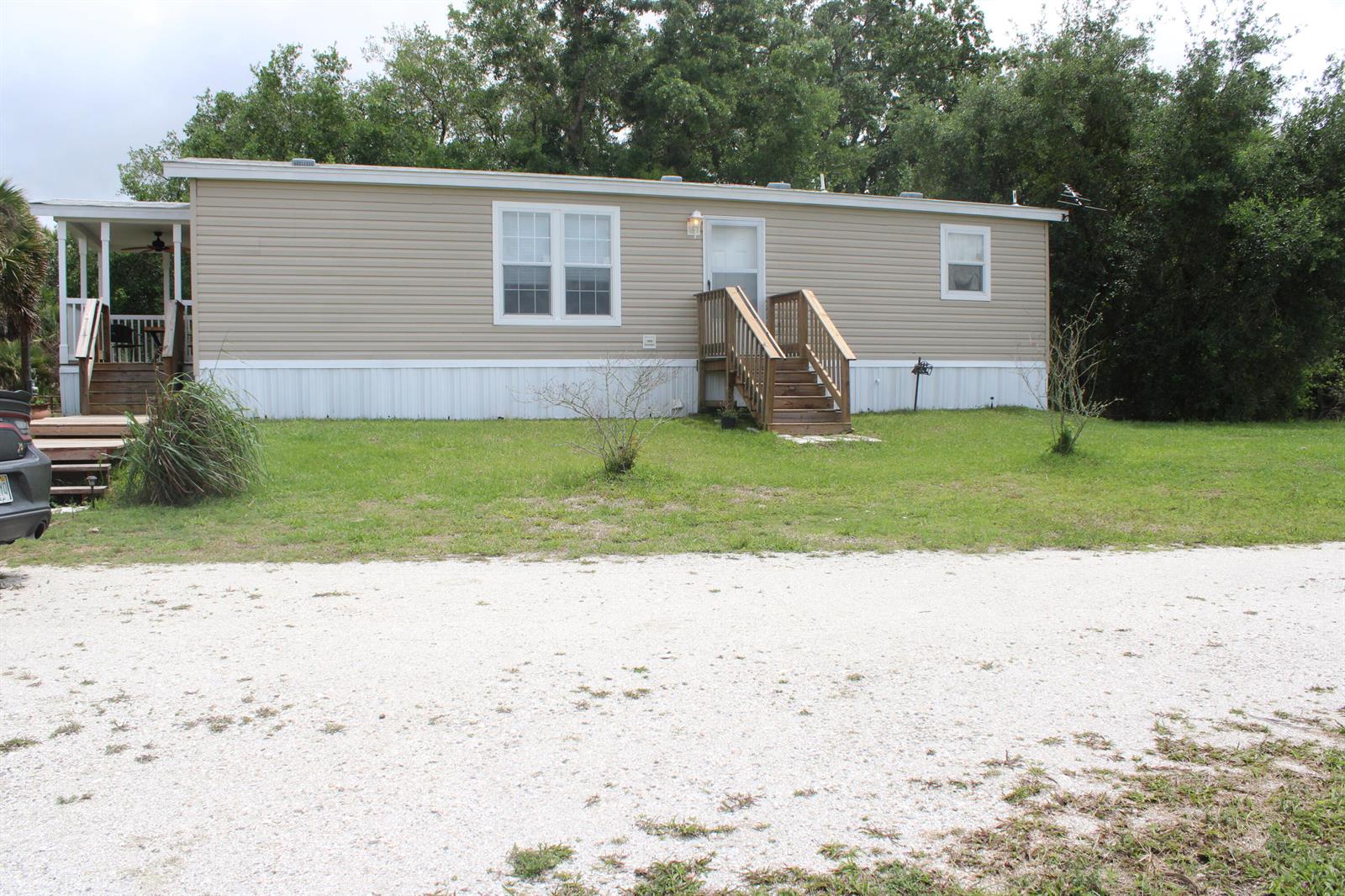 A tan mobile home with two wooden entry decks sits on a gravel lot — 15367 NW 296th Street, Okeechobee FL 34972, OKEECHOBEE, FL