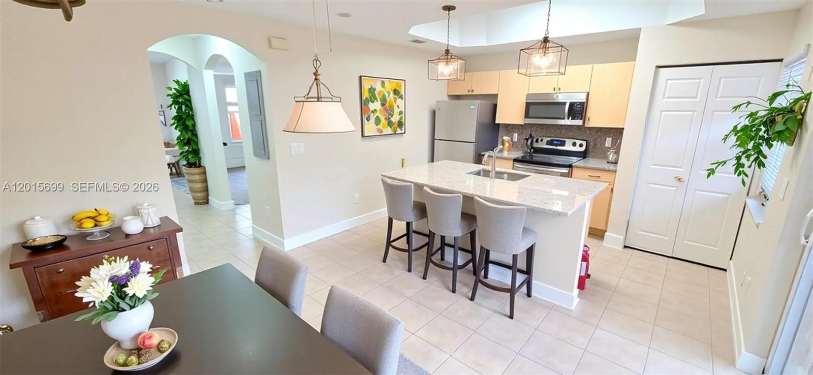 A kitchen features light wood cabinets, a granite-topped island with bar stools, and tile flooring — 4950 Tradewinds Ter # 505, Dania Beach FL 33312, DANIA BEACH, FL