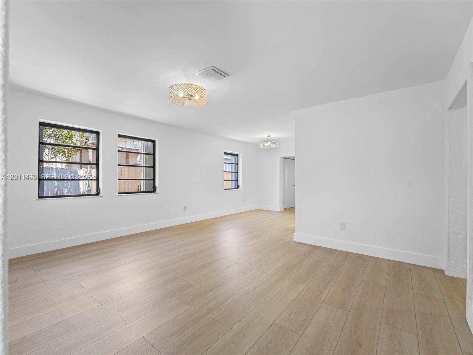 An empty room features white walls, light wood-look flooring, and two decorative ceiling light fixtures — 521 SW 64th Ct, Miami FL 33144, MIAMI, FL