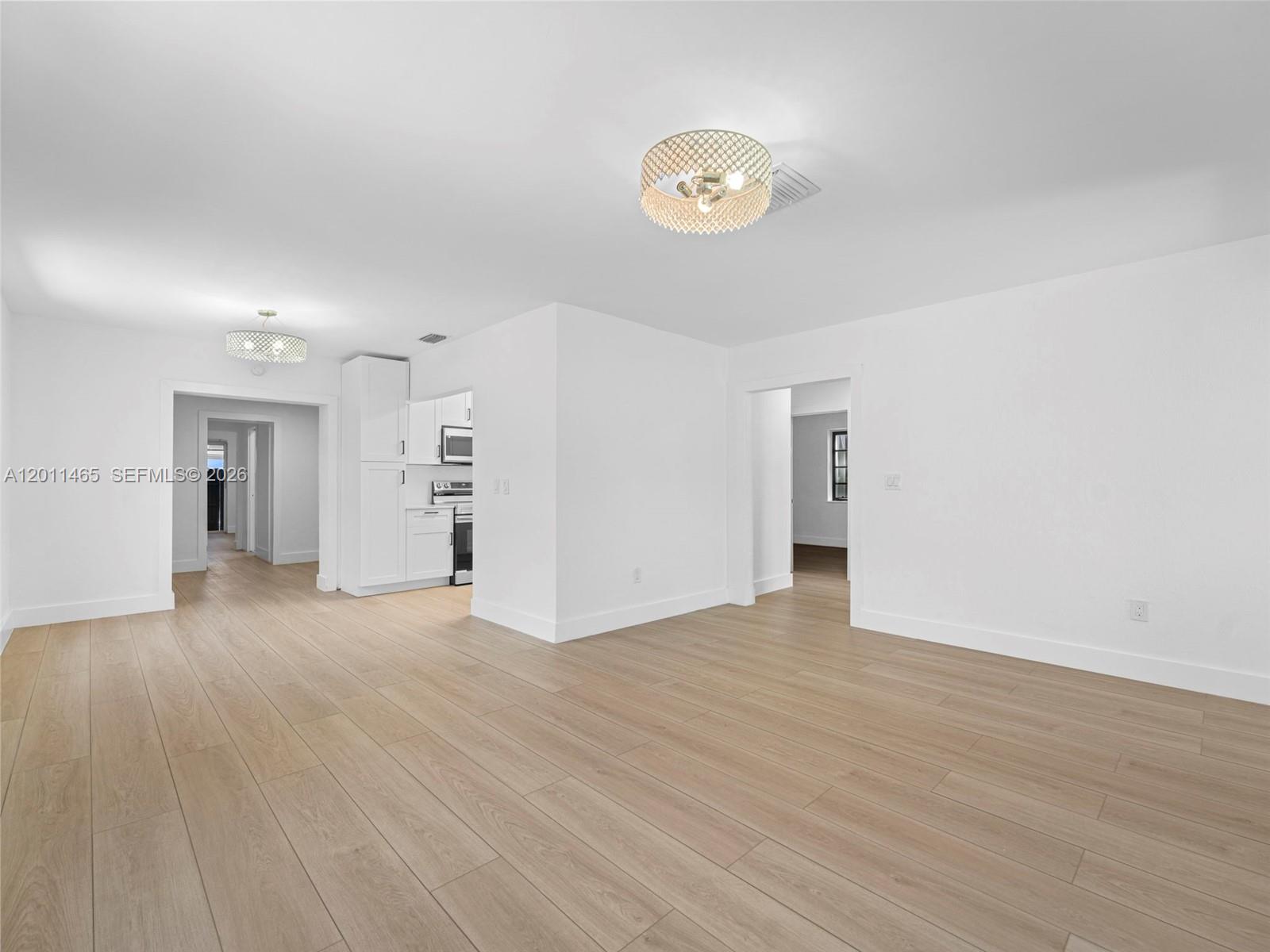 An open-concept room features light wood-look flooring, white walls, and two decorative ceiling light fixtures — 521 SW 64th Ct, Miami FL 33144, MIAMI, FL