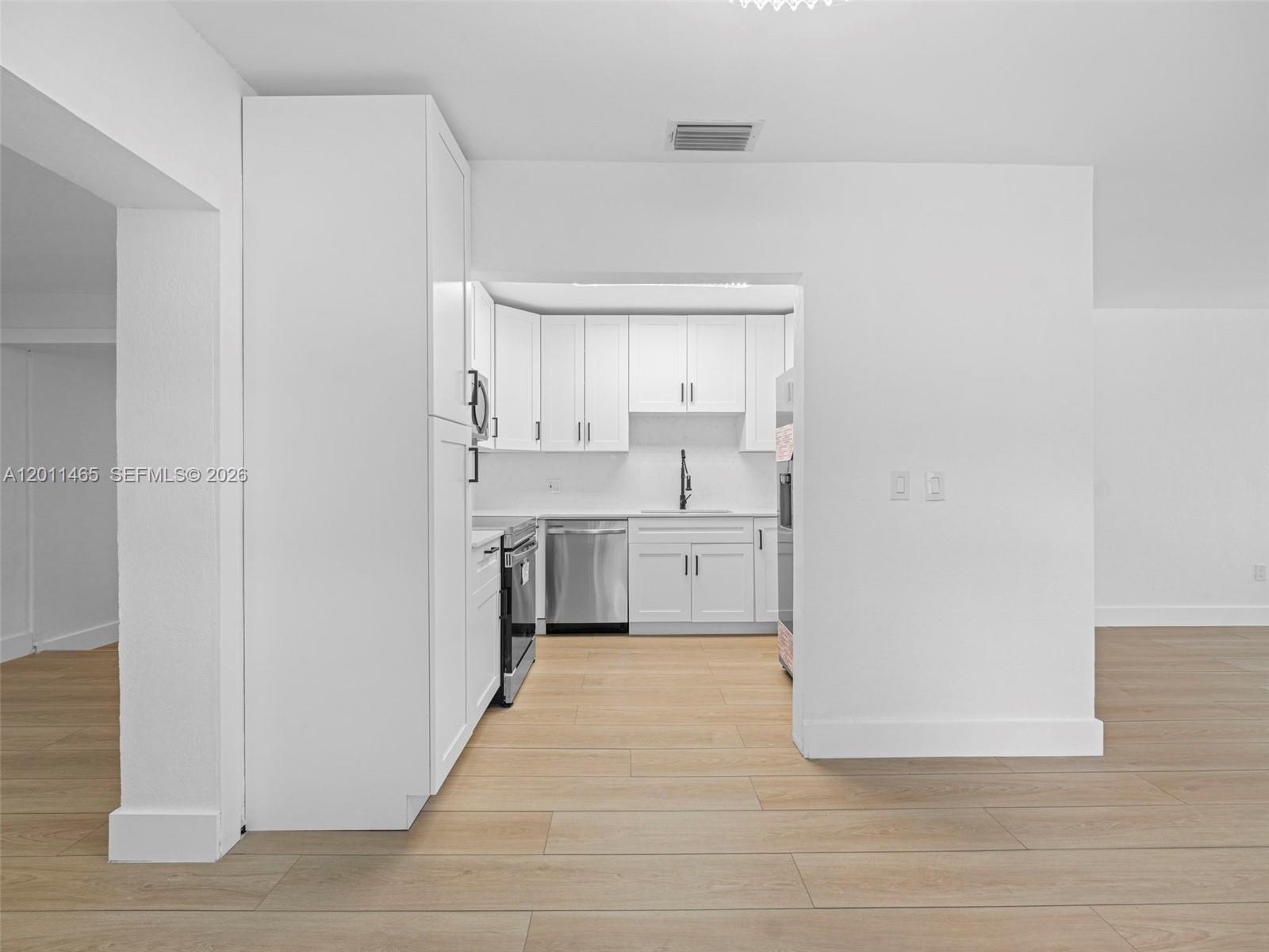 A white kitchen features stainless steel appliances and light wood-look flooring — 521 SW 64th Ct, Miami FL 33144, MIAMI, FL