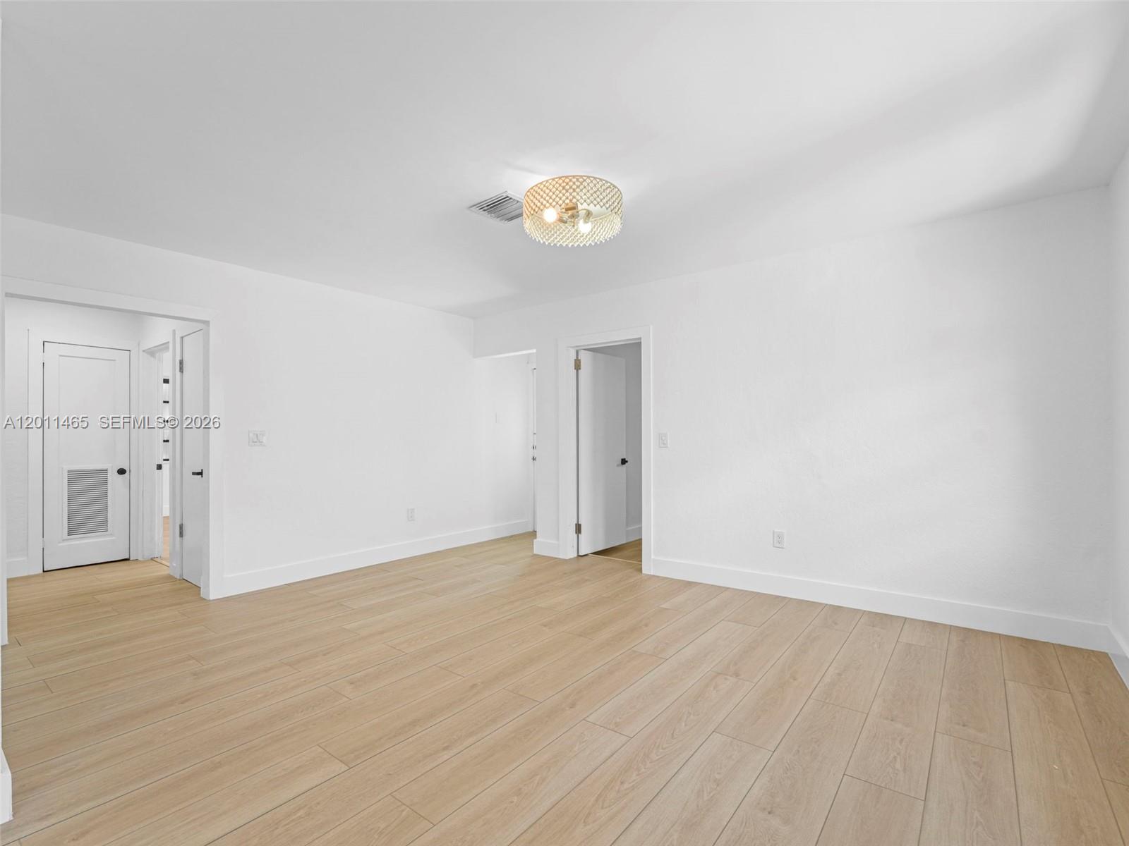 A bright, empty room features light wood-look flooring, white walls, and a decorative ceiling light — 521 SW 64th Ct, Miami FL 33144, MIAMI, FL