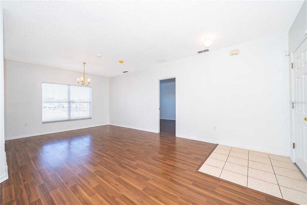 An empty room features wood-look flooring, a tiled entryway, a chandelier, and white walls — 213 BIG BLACK DRIVE, KISSIMMEE, FL
