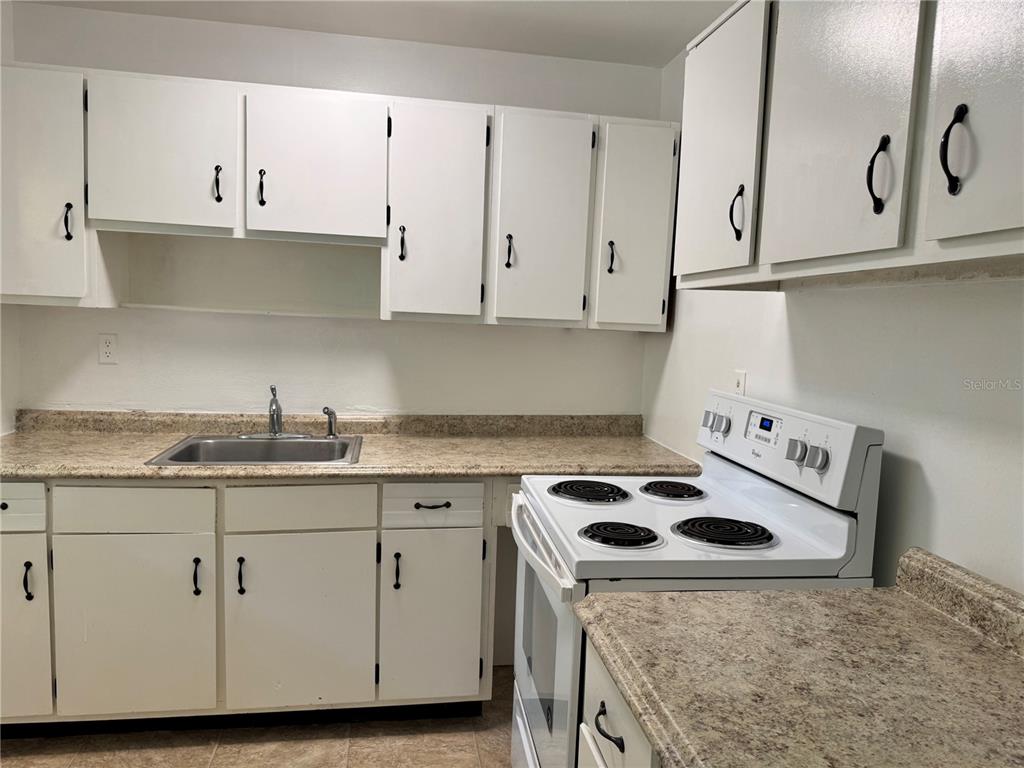 A kitchen features white cabinets, a stainless steel sink, and a white electric range — 921 NW 55TH TERRACE, GAINESVILLE, FL