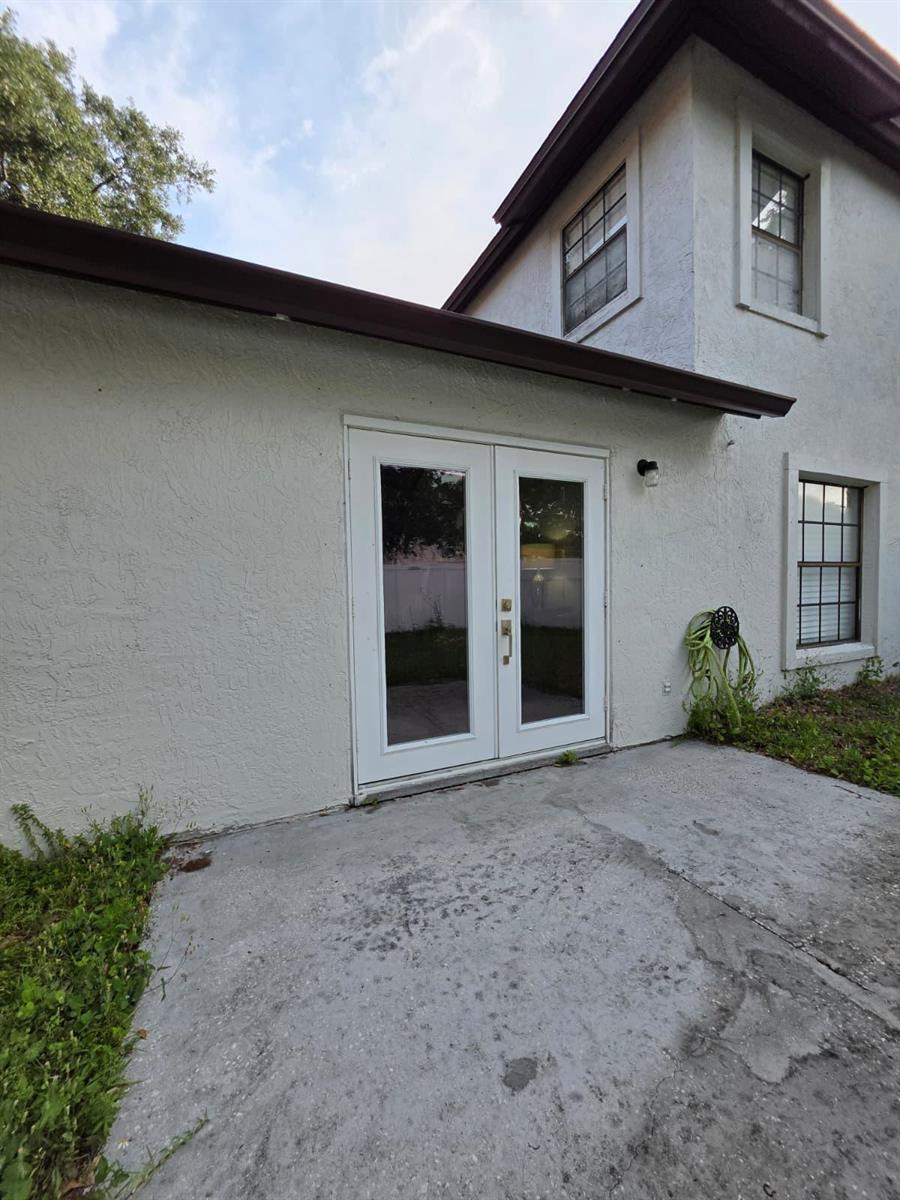 A white stucco house exterior features a set of double glass doors and a concrete patio — 3003 Pigeon Hawk Court, Orlando FL 32829, ORLANDO, FL