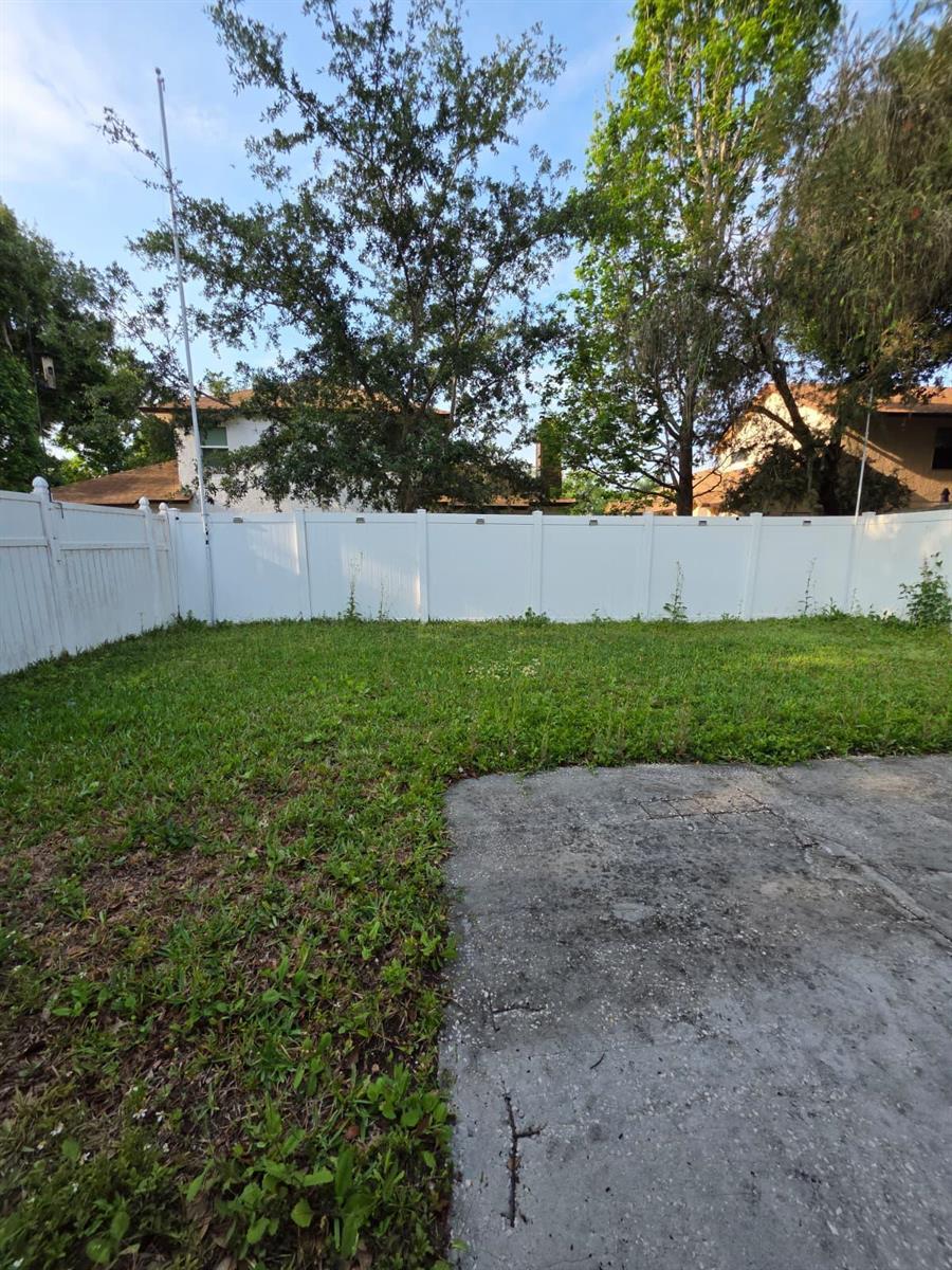 A fenced backyard features a concrete patio area and a grassy lawn with mature trees — 3003 Pigeon Hawk Court, Orlando FL 32829, ORLANDO, FL