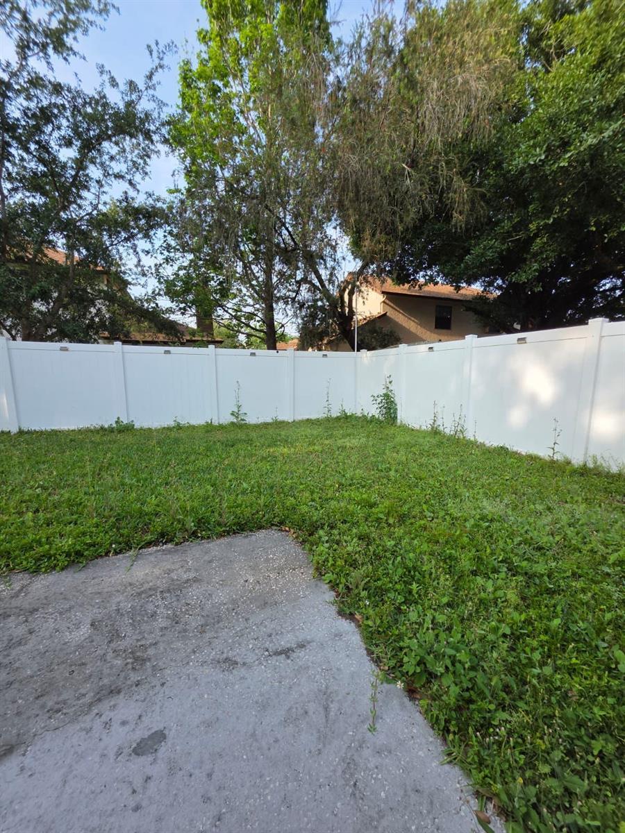 A backyard with a concrete patio, patchy grass, and a white vinyl privacy fence — 3003 Pigeon Hawk Court, Orlando FL 32829, ORLANDO, FL