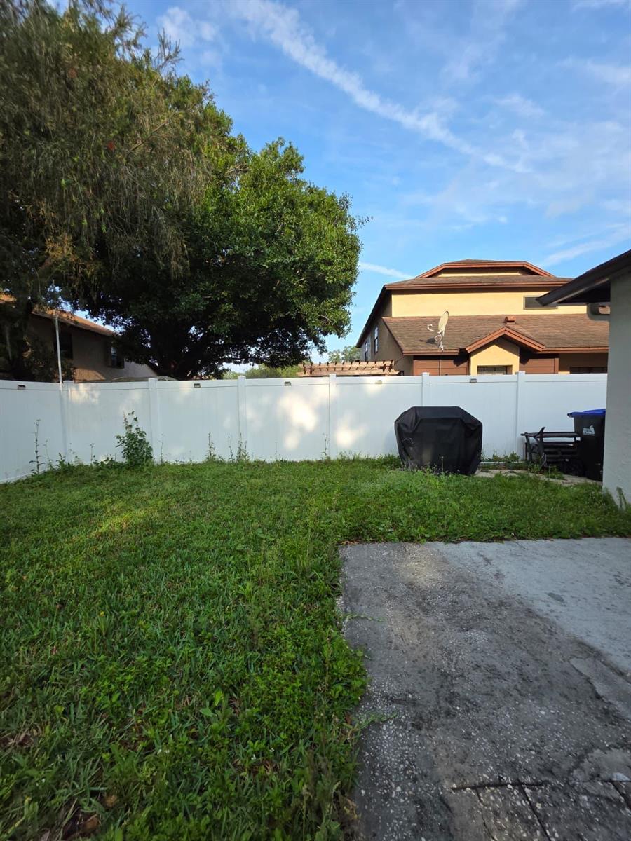 A fenced backyard features a patch of grass, a concrete patio, and a covered grill — 3003 Pigeon Hawk Court, Orlando FL 32829, ORLANDO, FL