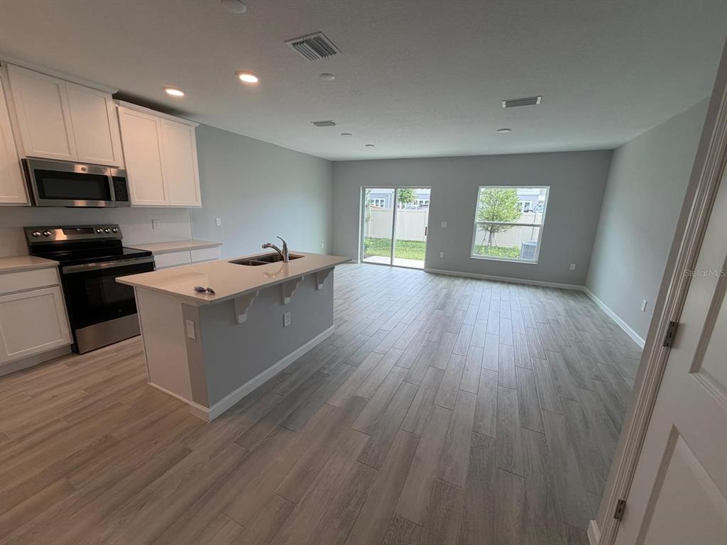A kitchen with white cabinets and an island opens into a living area with tile floors — 4152 CAMPSITE LOOP, ORLANDO, FL