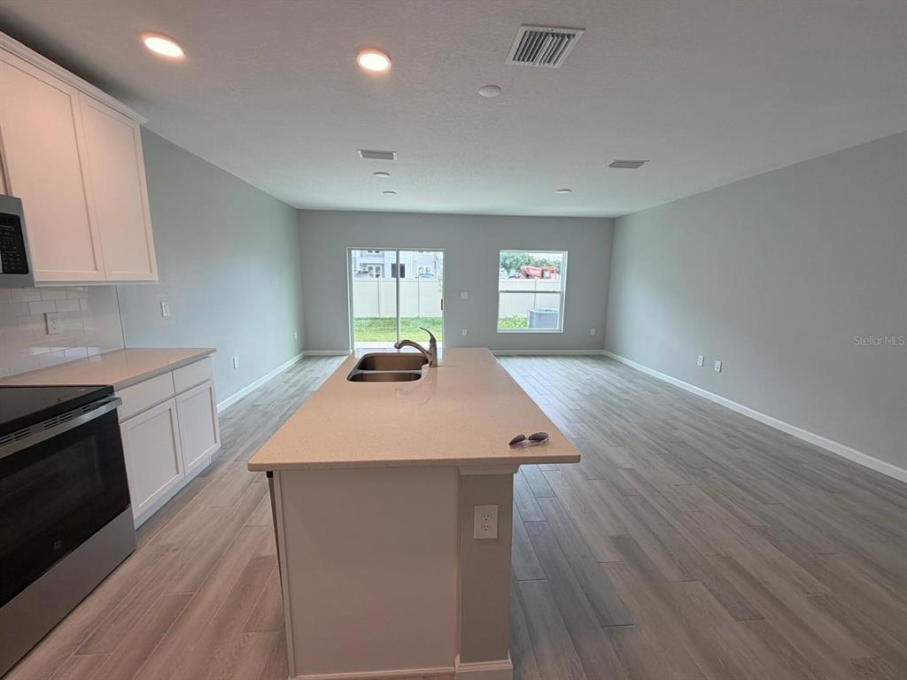 A kitchen with a central island, white cabinets, and light wood-look flooring — 4152 CAMPSITE LOOP, ORLANDO, FL