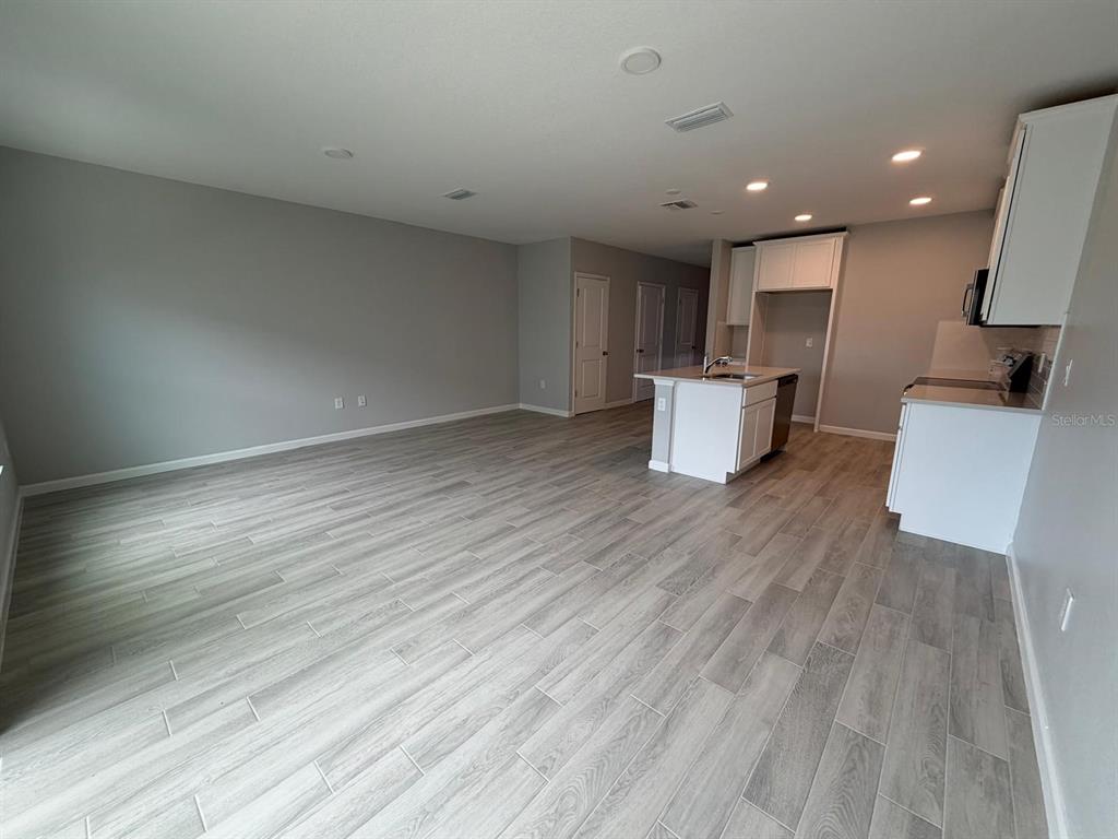 An open-concept kitchen and living area features light gray wood-look tile flooring and white cabinetry — 4152 CAMPSITE LOOP, ORLANDO, FL