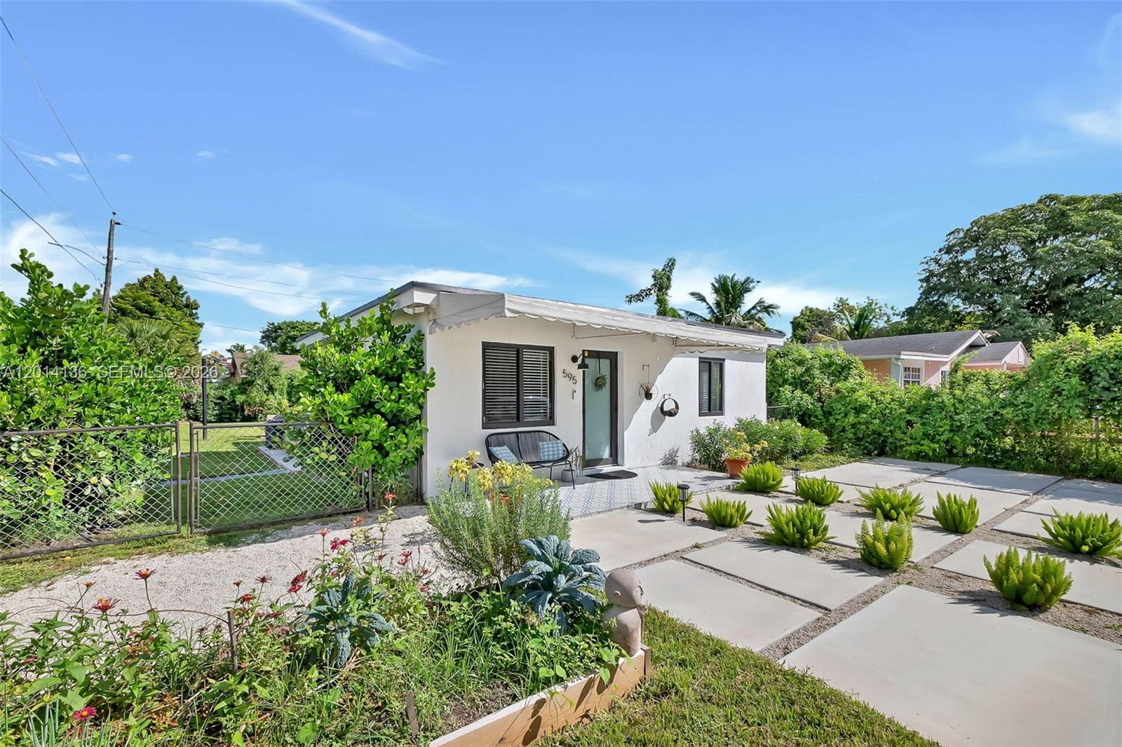 A white single-story house features a front patio with concrete pavers and a fenced yard — 595 NW 101st St, Miami FL 33150, MIAMI, FL