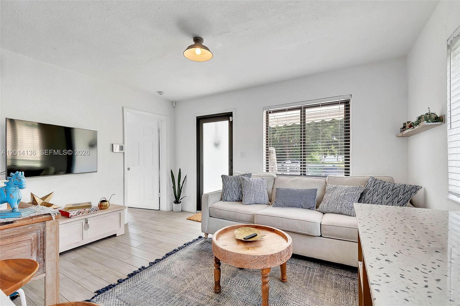 A bright living room features a beige sofa, a round wooden coffee table, and tile flooring — 595 NW 101st St, Miami FL 33150, MIAMI, FL