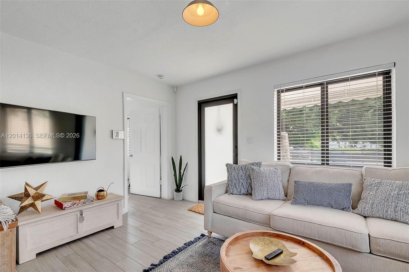 A living room features a beige sofa, a wooden coffee table, and a wall-mounted television — 595 NW 101st St, Miami FL 33150, MIAMI, FL