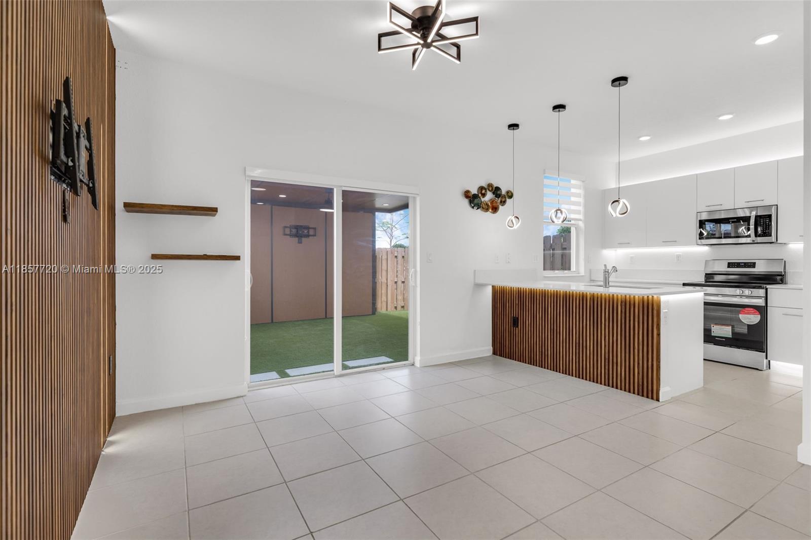 A modern kitchen and dining area features white cabinetry, wood-slat accents, and a sliding glass door — 12373 NW 24th Pl, Miami FL 33167, MIAMI, FL