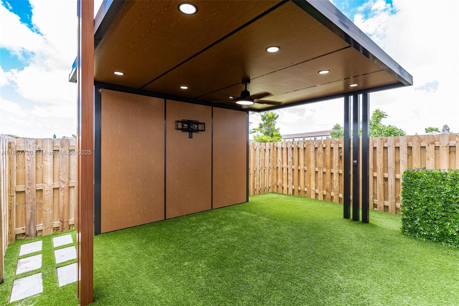 A covered outdoor patio features a wood-paneled wall, artificial turf, and a ceiling fan — 12373 NW 24th Pl, Miami FL 33167, MIAMI, FL