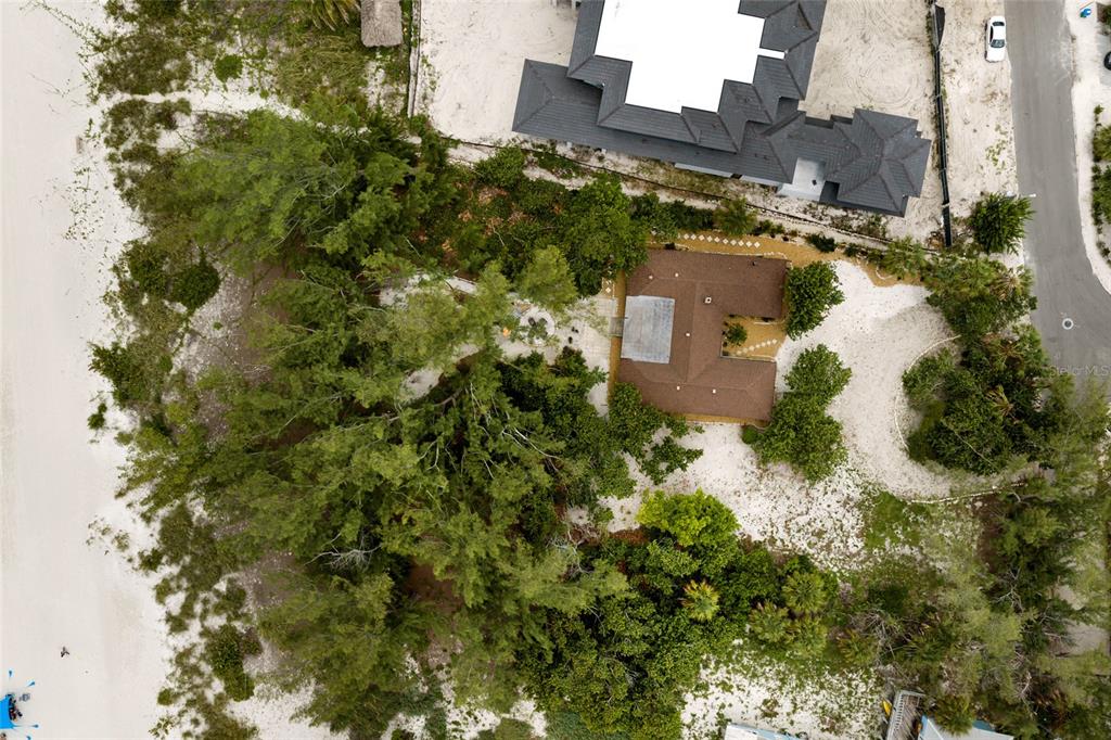 An aerial view shows a house surrounded by trees and sandy ground near a beach — 103 51ST STREET, BRADENTON BEACH, FL