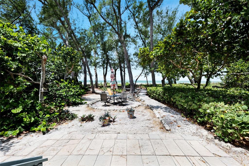 A paved patio leads to a sandy outdoor seating area surrounded by trees and foliage — 103 51ST STREET, BRADENTON BEACH, FL