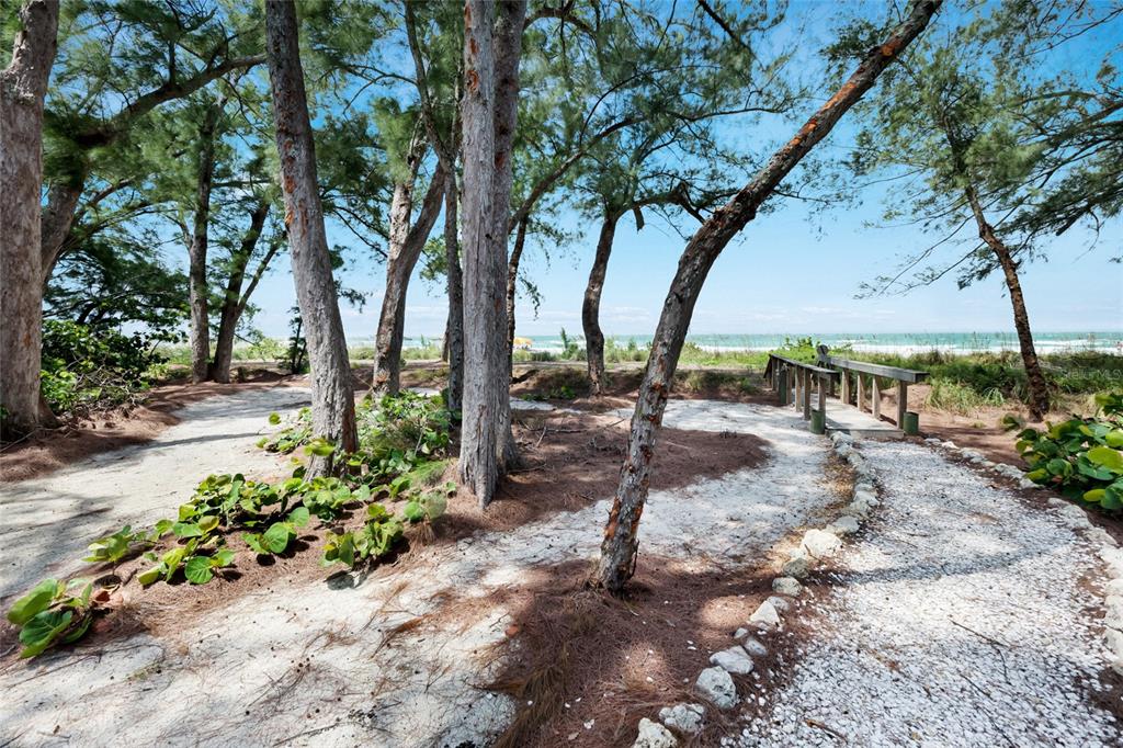 A sandy path leads through trees toward a wooden footbridge overlooking a beach and ocean — 103 51ST STREET, BRADENTON BEACH, FL