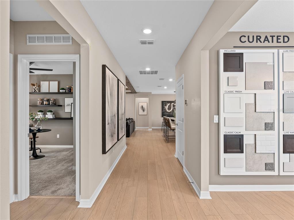 A hallway with light wood floors leads past a side room toward an open kitchen — 10770 LEAFY LAUREL STREET, ORLANDO, FL