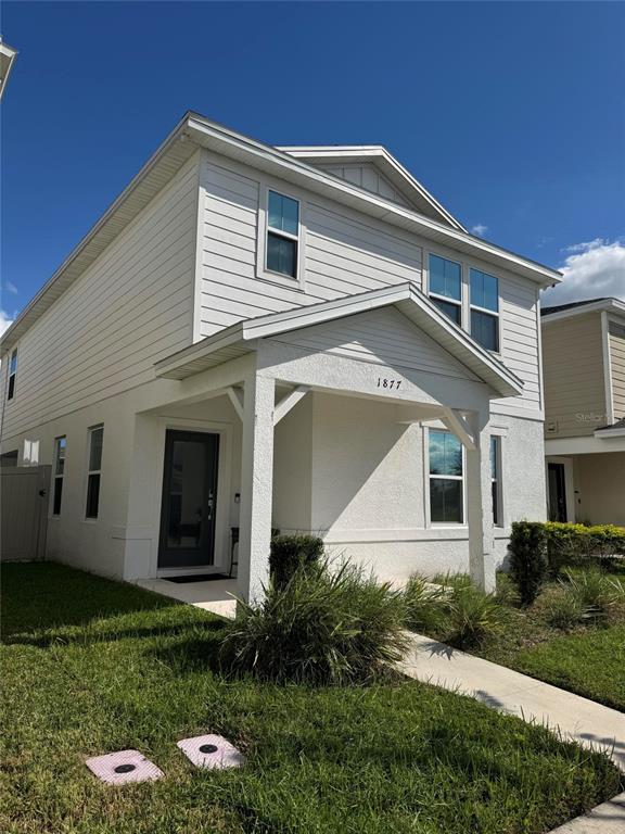 A two-story house with white siding and a covered front porch under a blue sky — 1877 SUMMER SERENITY DRIVE, KISSIMMEE, FL
