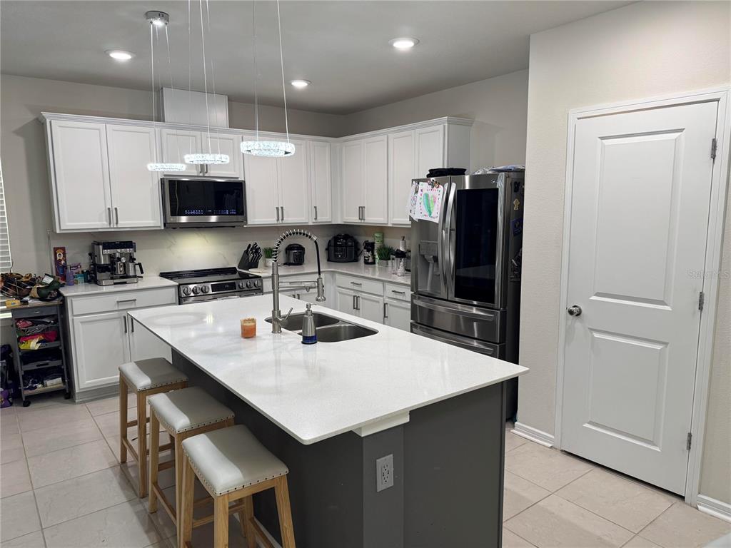 A kitchen features white cabinetry, a gray island with bar seating, and stainless steel appliances — 1877 SUMMER SERENITY DRIVE, KISSIMMEE, FL