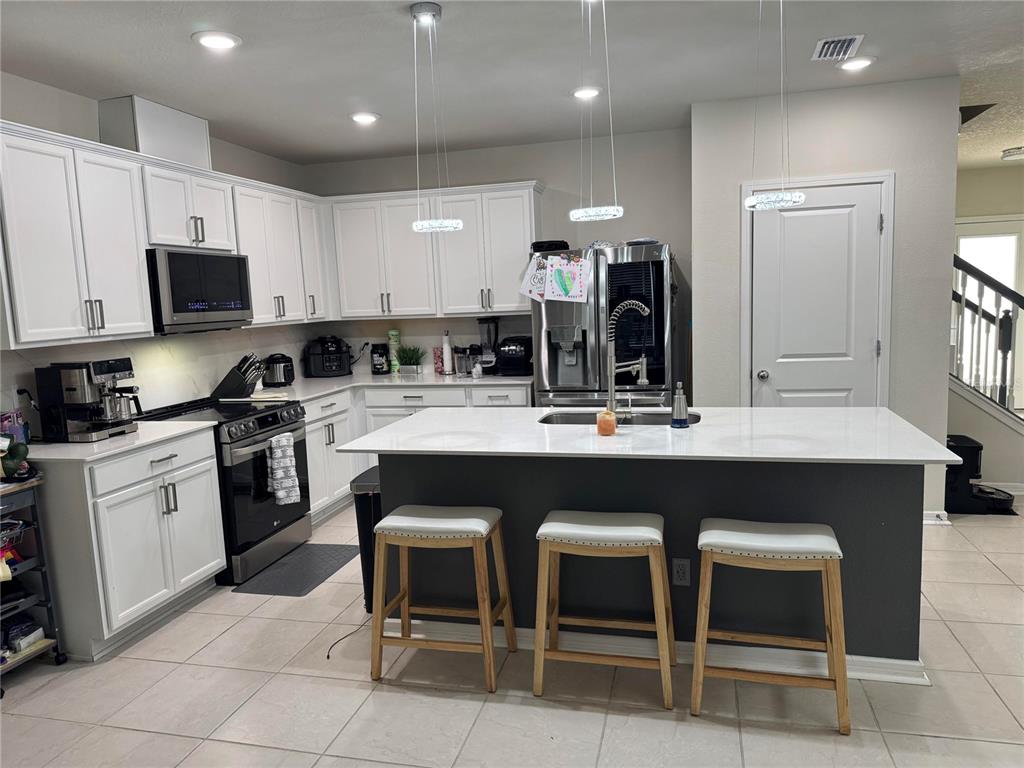 A kitchen features white cabinets, a dark gray island with three stools, and stainless appliances — 1877 SUMMER SERENITY DRIVE, KISSIMMEE, FL