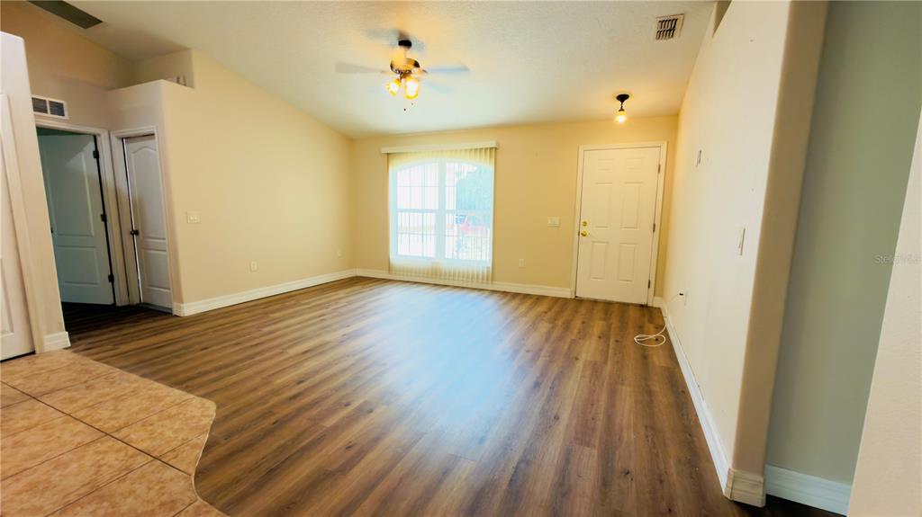 An empty living room features wood-look flooring, a ceiling fan, and a white entry door — 200 BREAKWATER STREET SE, PALM BAY, FL