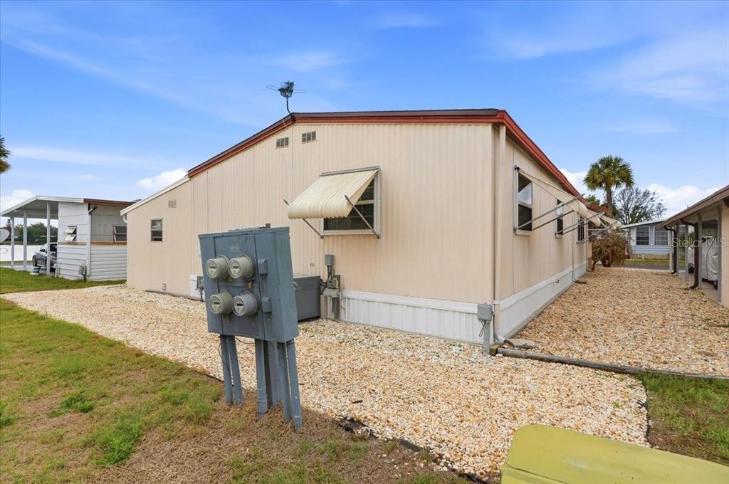 The exterior side of a mobile home features light-colored siding, metal awnings, and electrical meters — 4511 REDWOOD STREET, WINTER HAVEN, FL