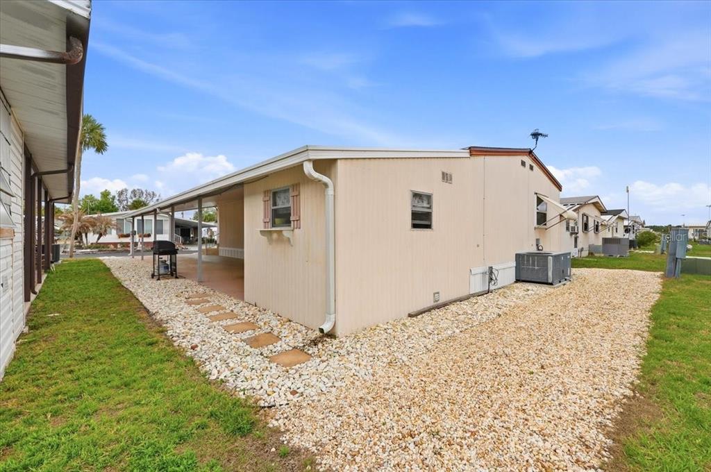 The exterior of a beige mobile home features a covered carport and gravel landscaping — 4511 REDWOOD STREET, WINTER HAVEN, FL