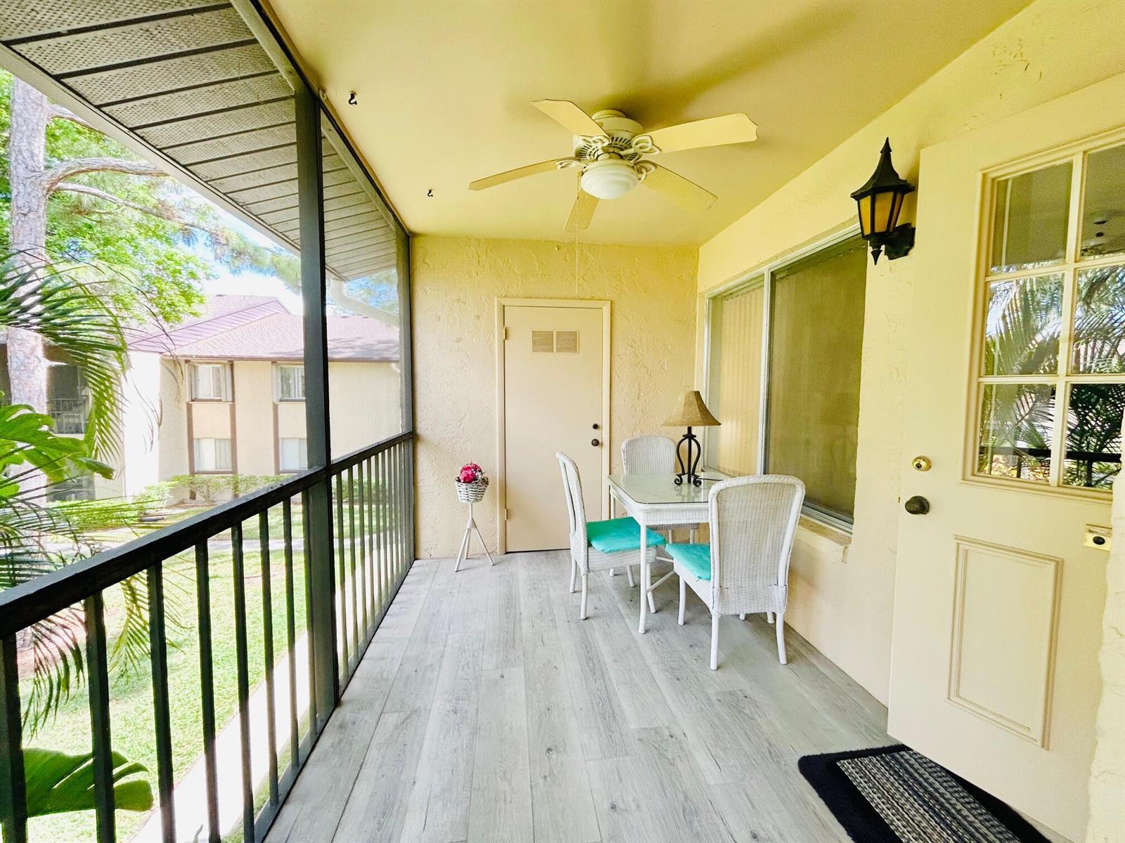 A screened-in porch features light wood-look flooring, a ceiling fan, and a small dining set — 408 Pine Glen Lane # 2, FL 33463, FL