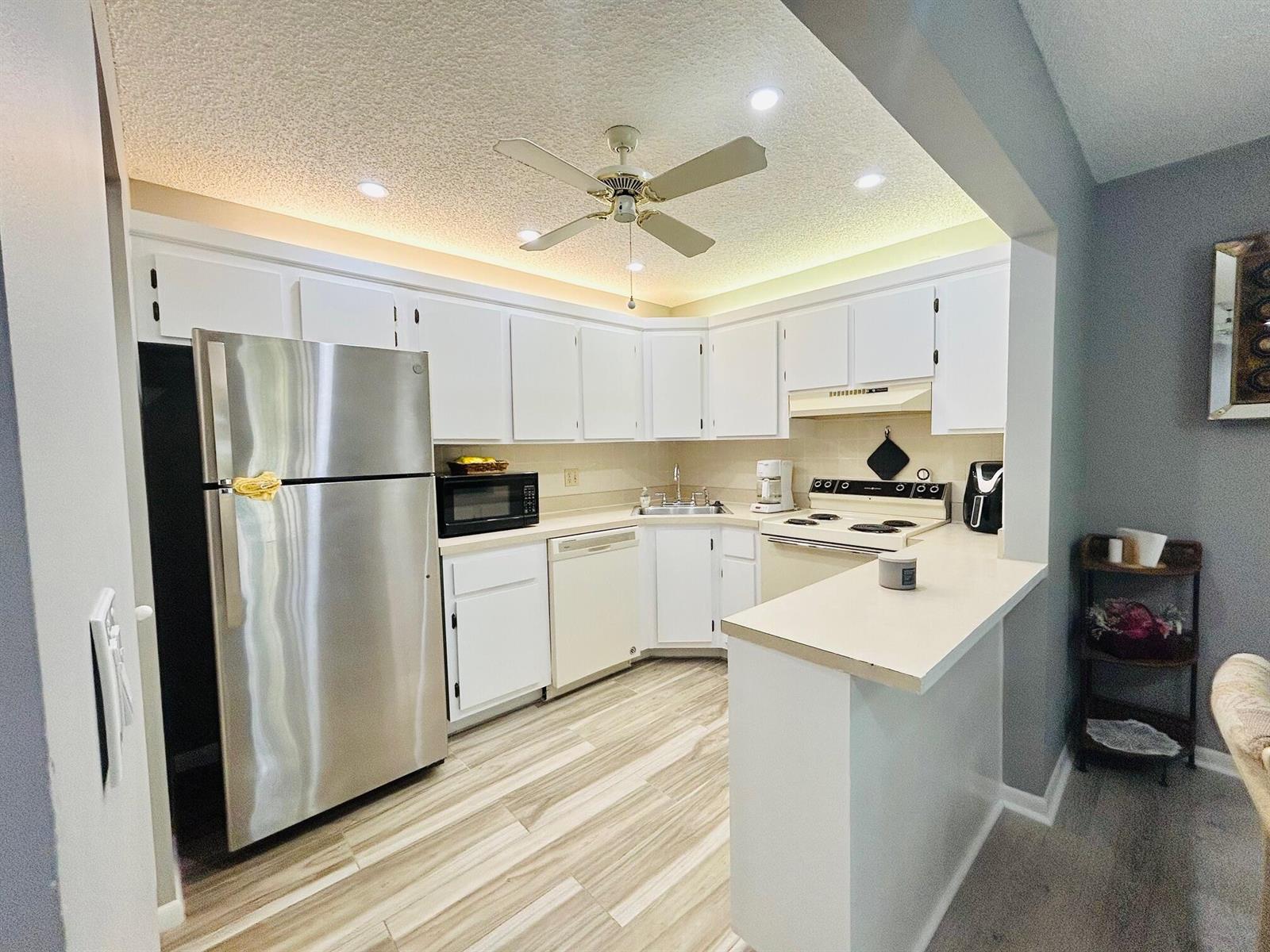 A kitchen features white cabinets, stainless steel appliances, a ceiling fan, and light wood-look flooring — 408 Pine Glen Lane # 2, FL 33463, FL