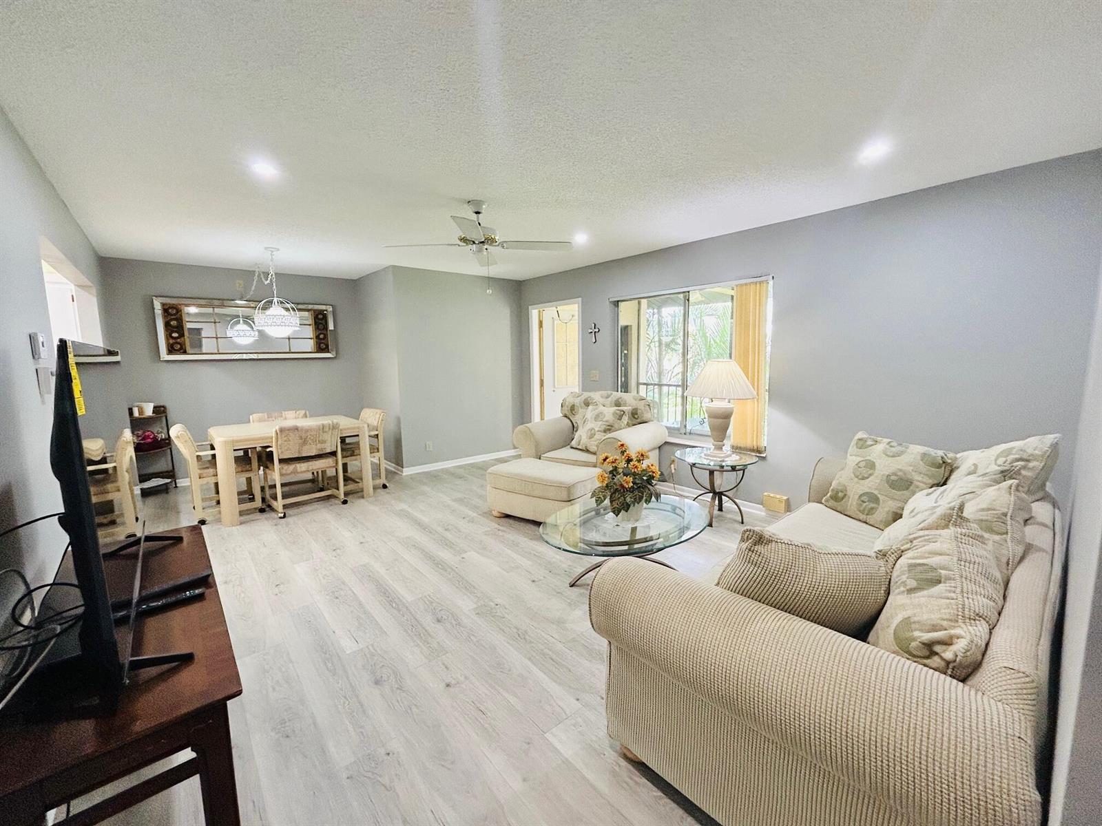 A living and dining room with light gray walls, wood-look flooring, and neutral furniture — 408 Pine Glen Lane # 2, FL 33463, FL