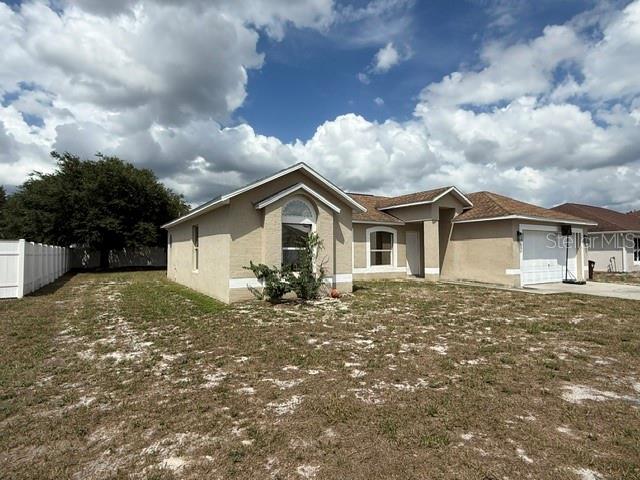A single-story tan house with a two-car garage and a large, sparse front yard — 1861 ASHTON PARK PLACE, ST CLOUD, FL