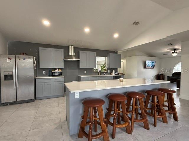 A kitchen features gray cabinets, a white island with four wooden stools, and stainless appliances — 1861 ASHTON PARK PLACE, ST CLOUD, FL