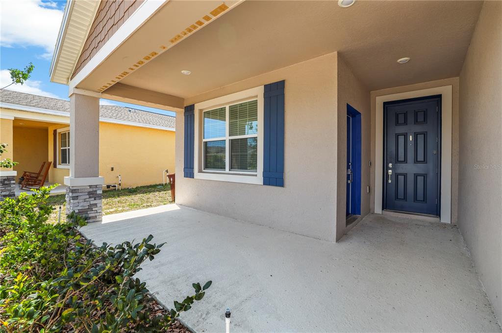 A covered concrete porch features a blue front door and a window with blue shutters — 1259 LASSEN STREET, HAINES CITY, FL