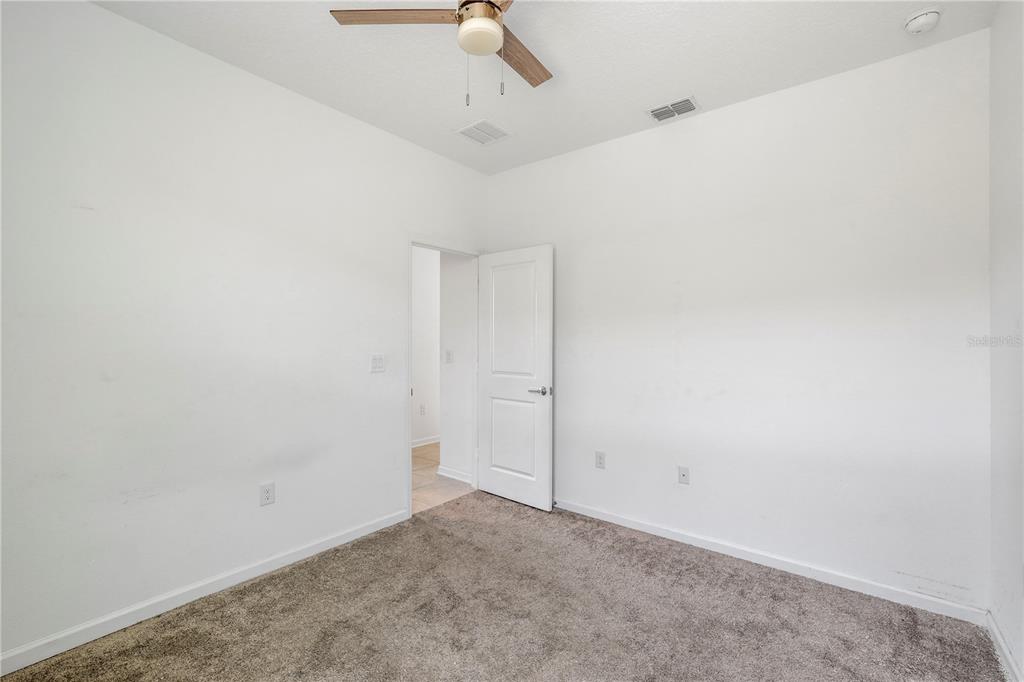 An empty bedroom features white walls, gray carpeting, a ceiling fan, and an open doorway — 1259 LASSEN STREET, HAINES CITY, FL