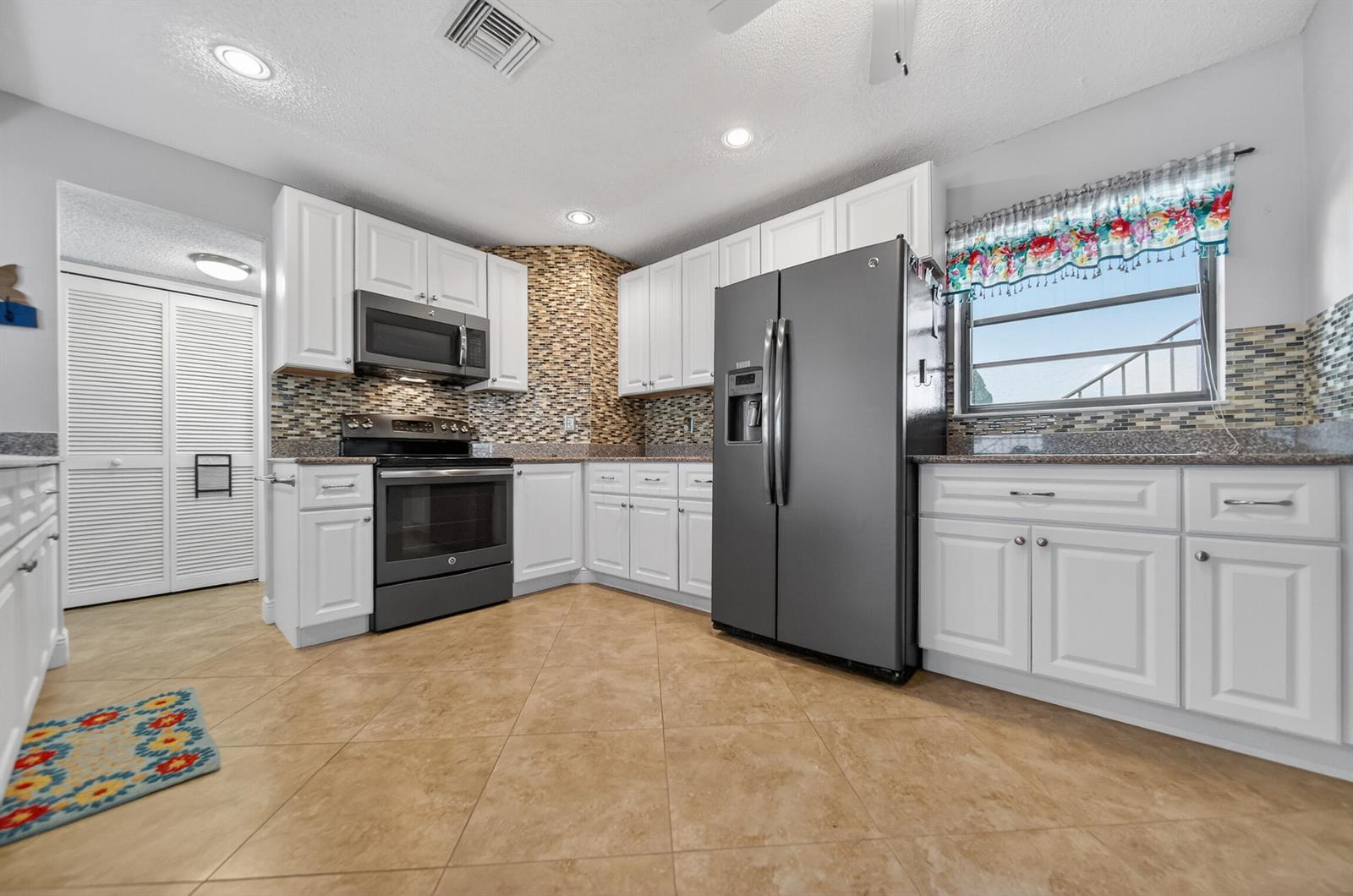 A kitchen features white cabinetry, dark appliances, a mosaic tile backsplash, and tan floor tiles — 4083 SE Centerboard Lane # a, Stuart FL 34997, STUART, FL