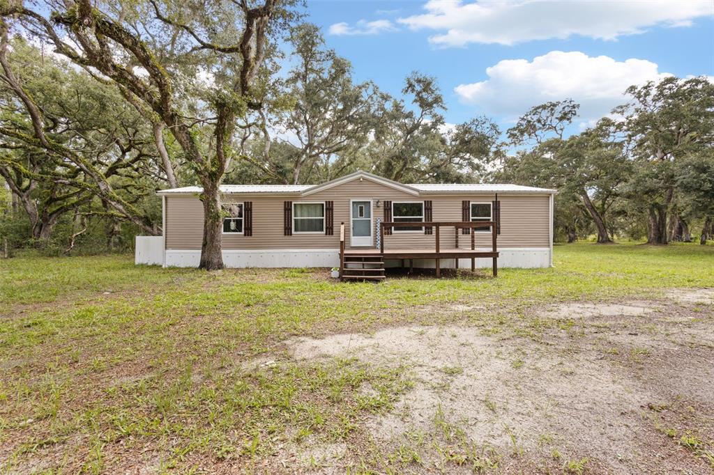 A single-story manufactured home with tan siding and a wooden deck sits among trees — 11 NE 434TH STREET, OLD TOWN, FL