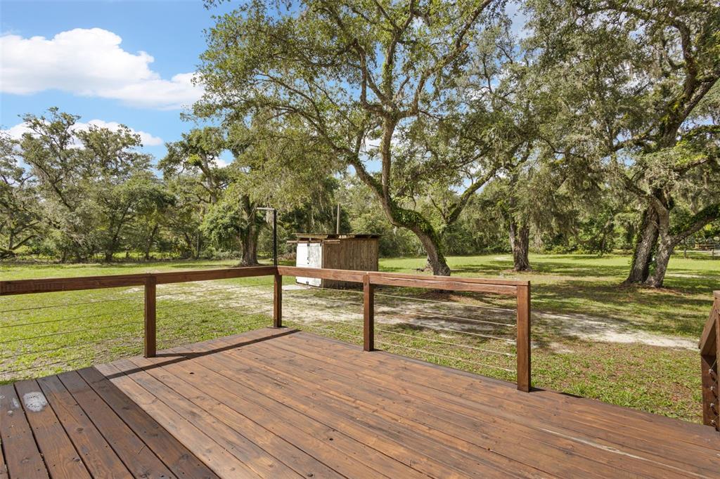 A wooden deck with a cable railing overlooks a grassy yard with large oak trees — 11 NE 434TH STREET, OLD TOWN, FL