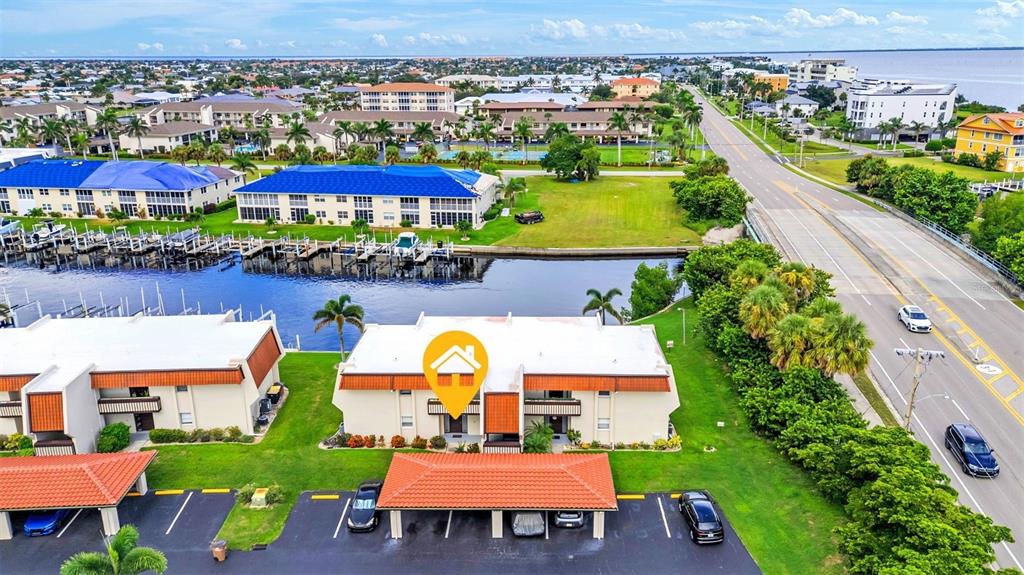 An aerial view shows a multi-story residential building with a covered parking area and canal — 311 GARVIN STREET UNIT 205A, PUNTA GORDA, FL