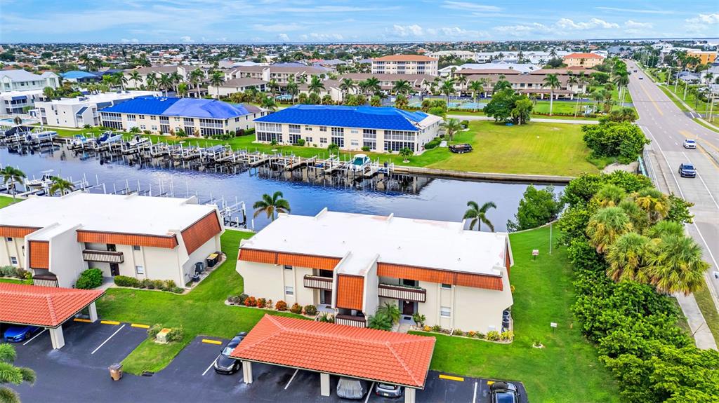 An aerial view shows multi-story apartment buildings with red-tiled roofs alongside a canal with boat slips — 311 GARVIN STREET UNIT 205A, PUNTA GORDA, FL