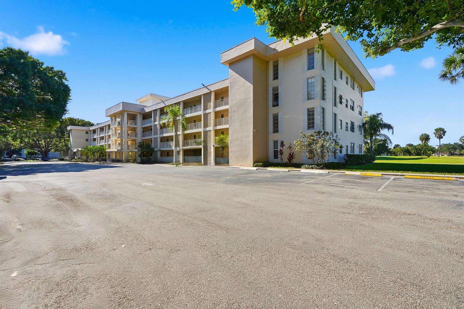 A multi-story apartment building with balconies stands next to a large, empty asphalt parking lot — 2601 S Course Drive # 202, Pompano Beach FL 33069, POMPANO BEACH, FL