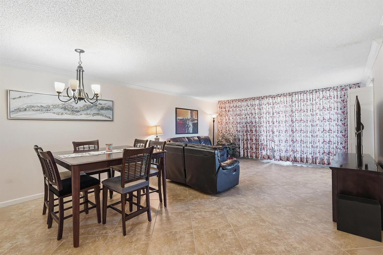 An open-concept living and dining area features tile flooring, a chandelier, and floor-to-ceiling curtains — 2601 S Course Drive # 202, Pompano Beach FL 33069, POMPANO BEACH, FL