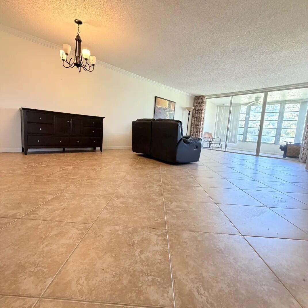 A spacious living room features large beige floor tiles, a dark dresser, and sliding glass doors — 2601 S Course Drive # 202, Pompano Beach FL 33069, POMPANO BEACH, FL