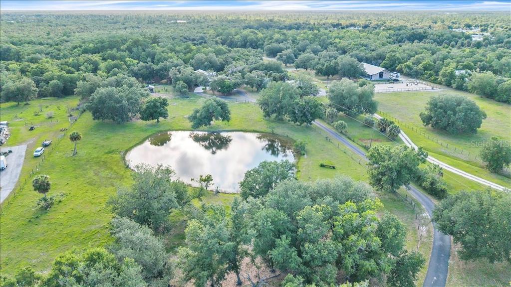 An aerial view shows a pond surrounded by grassy fields, trees, and a house — 10597 SW KISSIMMEE ROAD, ARCADIA, FL