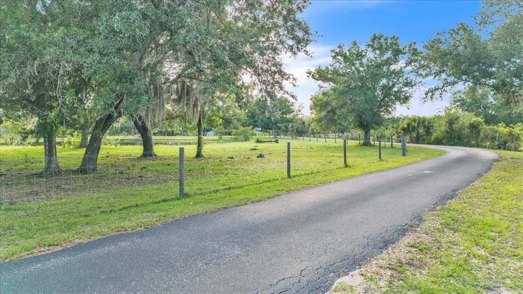 A paved driveway curves past a fenced grassy field with large trees and a pond — 10597 SW KISSIMMEE ROAD, ARCADIA, FL