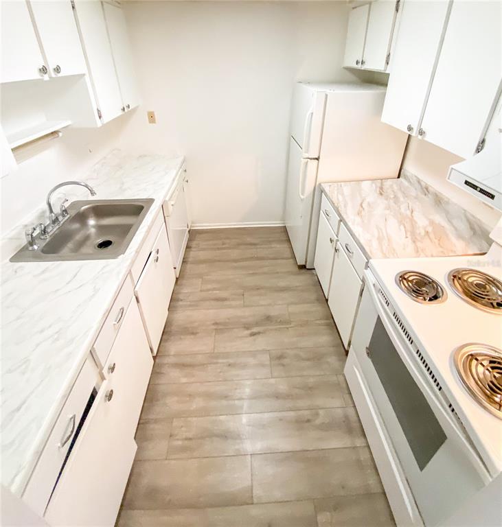A galley kitchen features white cabinets, marble-patterned countertops, white appliances, and wood-look flooring — 4335 AEGEAN DRIVE UNIT 108A, TAMPA, FL
